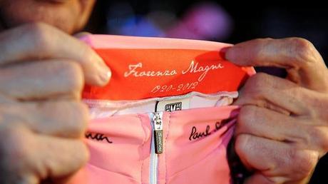 Maglia rosa per il Giro d’Italia 2013 presentata a Milano e dedicata alla memoria di Fiorenzo Magni, il grande campione del ciclismo scomparso di recente. La dedica è all’interno del colletto: autografo e le date 1920-2012. La maglia rosa è ancora prodotta dal Maglificio Santini e disegnata da Paul Smith. Oltre alla firma dello stilista britannico, presente sul colletto delle maglie, sarà presente anche il bordino multi stripe sulla manica sinistra come marchio di fabbrica di Paul Smith.  A Milano presentate la maglia rosa e quelle rossa, blu e bianca  La maglia rosa è come sempre la grande protagonista visto che sarà lei a distinguere in gruppo il leader della classifica generale. Gli altri colori sono il rosso (classifica a punti), il blu (scalatori) e bianca (miglior giovane). Perché Rcs Sport ha scelto Paul Smith per disegnare la maglia rosa? “Essendo io stesso, ormai da molti anni, un grandissimo appassionato di ciclismo, è stato per me un assoluto privilegio ricevere questo invito a disegnare le maglie del Giro d’Italia”, ha spiegato lo stilista britannico che documenta sul suo blog la passione per i pedali.  All’interno del colletto della maglia rosa la dedica a Fiorenzo Magni  Maglia rosa con molti elementi rossi di contorno: l’orlo della manica destra, l’outline laterale del pannello frontale e il bordo inferiore oltre l’interno del colletto con la firma di Magni. Ovviamente una scelta dovuta all’inserimento nel design del main sponsor Balocco che negli anni scorsi abbiamo visto sulla maglia rosa away della Juventus. Per quanto riguarda le altre maglie del Giro d’Italia 2013 da segnalare ancora il rosso al posto del tradizionale ciclamino per la classifica generale e il blu al posto del verde per il leader degli scalatori. La domanda è la stessa del 2012: perché cambiare?