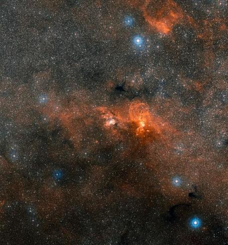 L'immagine a grande campo, basata su dati della DSS2 (Digitized Sky Survey 2), mostra l'intera regione che circonda la fabbrica cosmica NGC 3603, a circa 20000 anni luce di distanza dalla Terra. Questa zona contiene un notevole numero di regioni di formazione stellare con enormi nubi di gas risplendente. Crediti: ESO/Digitized Sky Survey 2