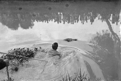 Città del Messico, Lago Xochimilco, 1960: Il corpo di un uomo assassinato è scaricato nel canale Xochimilco. Un soccorritore legato a un cavo di sicurezza si occupa del recupero. Sulla sponda opposta, una folla di curiosi.