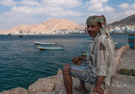 Un pescatore yemenita con, alle spalle, i tipici pescherecci locali