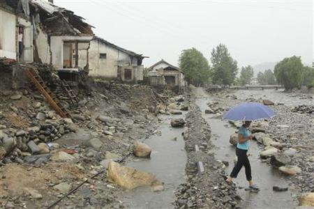 Una donna in possesso di un ombrello, passa davanti vicino alle case danneggiate dal recente alluvione nel distretto Kujang, nella provincia di Nord Pyongan, 28 agosto 2012.  REUTERS / Mission East / Comunicato stampa