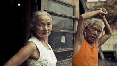 Noriko Shinohara (l.) looks in the camera as her husband Ushio stretches. From Zachary Heinzerling’s CUTIE AND THE BOXER, a documentary about the 40-year marriage of artists Ushio and Noriko Shinohara. Photo credit: Erik Jonsso