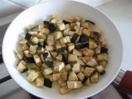 Lavare e tagliare la melanzana a quadrotti, in una padella aggiungere un pò d'olio extravergine d'oliva (4 cucchiai), farlo leggermente riscaldare e aggiungere le melanzane ( le melanzane assorbiranno l'olio, quindi bisogna aggiungere un pò di acqua tiepida e far cuocere per circa 10 minuti a coperchio chiuso).