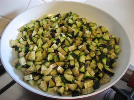 Lavare e tagliare le zucchine e le melanzane a cubetti. In una padella far imbiondire leggermente la cipolla tagliata a pezzettini in 4 cucchiai di olio extravergine d'oliva. Aggiungere gli ortaggi e un bicchiere di acqua tiepida.