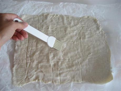 Stendere il rotolo di pasta sfoglia tra 2 fogli di carta da forno. Togliere un foglio e con un pennello spalmare la superficie con un pò di acqua.