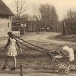 Piccola bambina passeggia la sorellina nel passeggino a mano libera. Ci pensano le trecce.