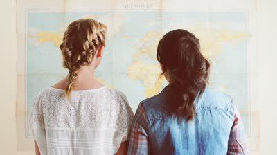stock-footage-tourist-girls-looking-at-world-map-planning-travel-adventure