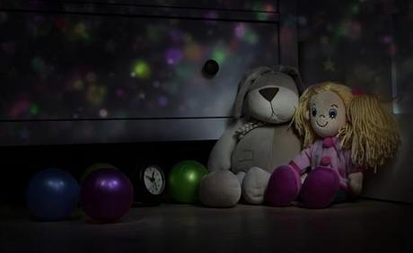 Doll and Teddy rabbit, watches and balls on  floor in the children's room at night. Toys in a dark room.