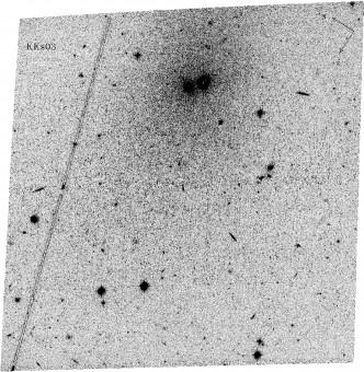 Immagine in negativo della galassia nana KKs 3, realizzata dalla Advanced Camera for Surveys a bordo del telescopio spaziale Hubble. Il nucleo della galassia è individuato dalla zona di destra dell'oggetto scuro in alto al centro della ripresa, con le sue stelle che si distribuiscono tutt'attorno in un'ampia zona (la zona scura di sinistra è invece un ammasso globulare di stelle molto più vicino a noi). Crediti: D. Makarov