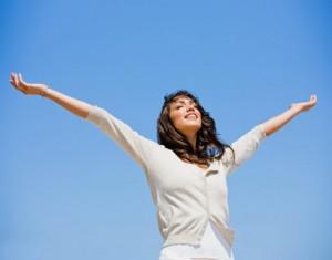 Pretty young woman with arms raised against blue sky