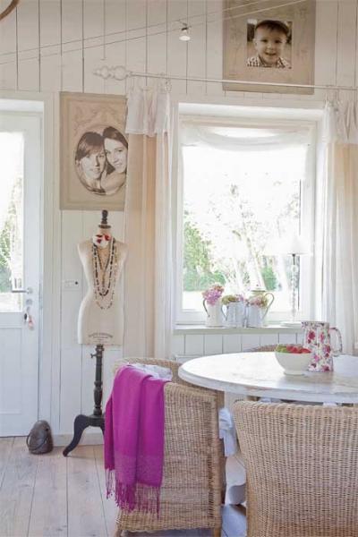 Ściany z pomalowaną na biało boazerią, stare kufry podróżne i wiklinowe fotele wprowadzają wakacyjny klimat. Ellen okrasiła dom kobiecymi dodatkami.