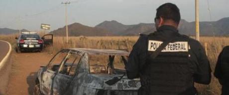 Federal police stand next to a bullet riddled and burned car after a criminal gang ambushed a police convoy near the town of Soyatlan, near Puerto Vallarta, Mexico, Monday, April 6, 2015. According to the Jalisco state prosecutors office, at least 15 state policed officers were killed and five others wounded, the single deadliest attack on Mexican police in recent memory. (ANSA/AP Photo)