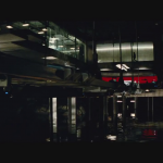 09 - Bruce Wayne passeggia in un corridoio sopra quella che sembra la sua Bat Caverna. Ci sono dei veicoli parcheggiati (tra cui forse la Batmobile). Notare nel cerchio un enigmatico costume protetto in una teca. Potrebbe essere appartenuto a Robin.