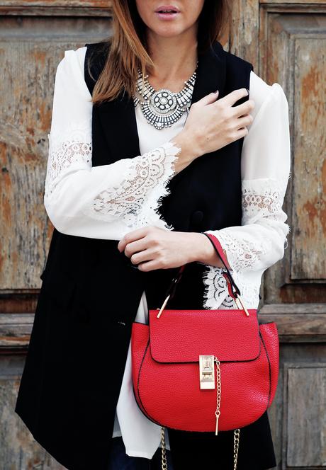 Top bianco con maniche in pizzo, gilet nero e borsa rossa