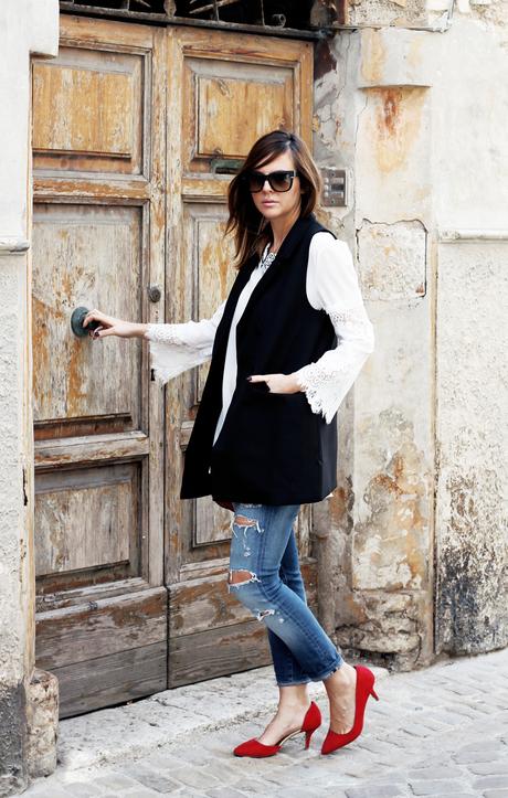 Top bianco con maniche in pizzo, gilet nero e borsa rossa