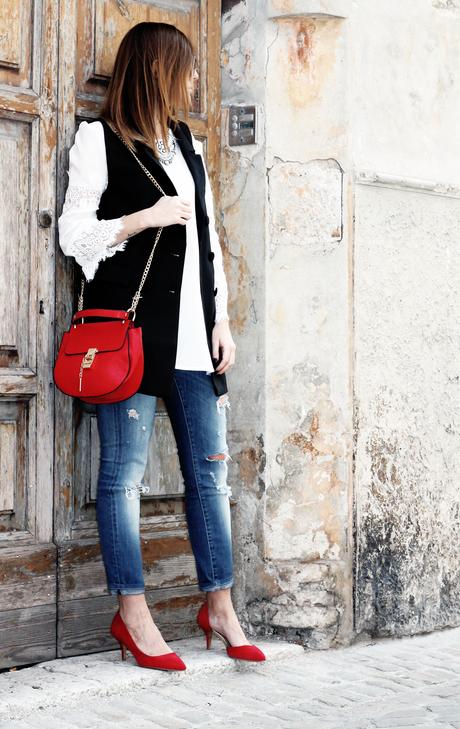 Top bianco con maniche in pizzo, gilet nero e borsa rossa