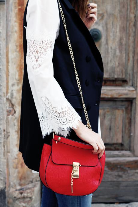 Top bianco con maniche in pizzo, gilet nero e borsa rossa