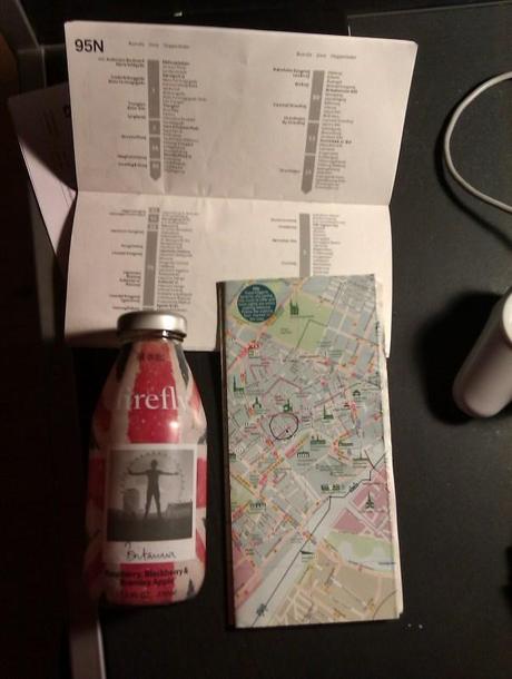 Una foto di una cartina di Copenhagen, di un libretto degli autobus notturni ed una bottiglietta di “Firefly”